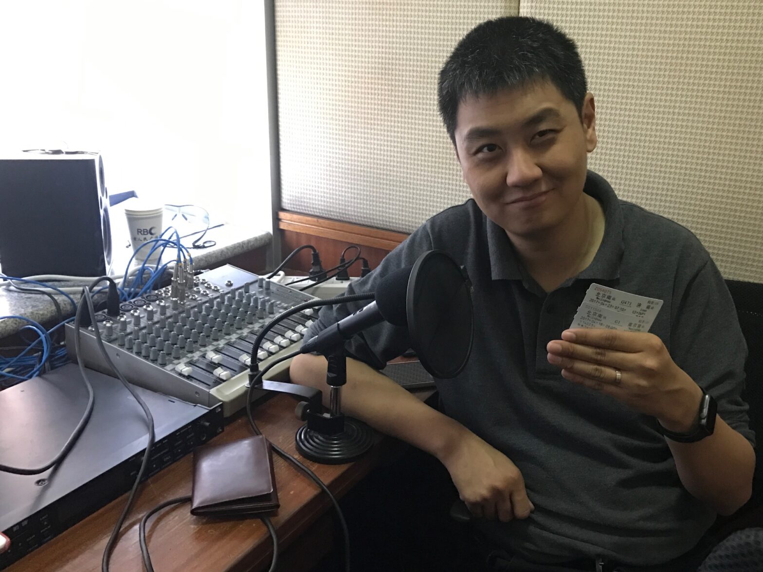 A picture of David Feng holding two railway tickets in front of an audio recording microphone
