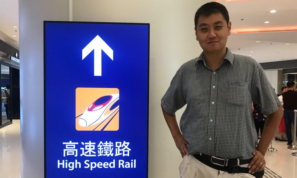 An image of David Feng with an HSR sign in Hong Kong